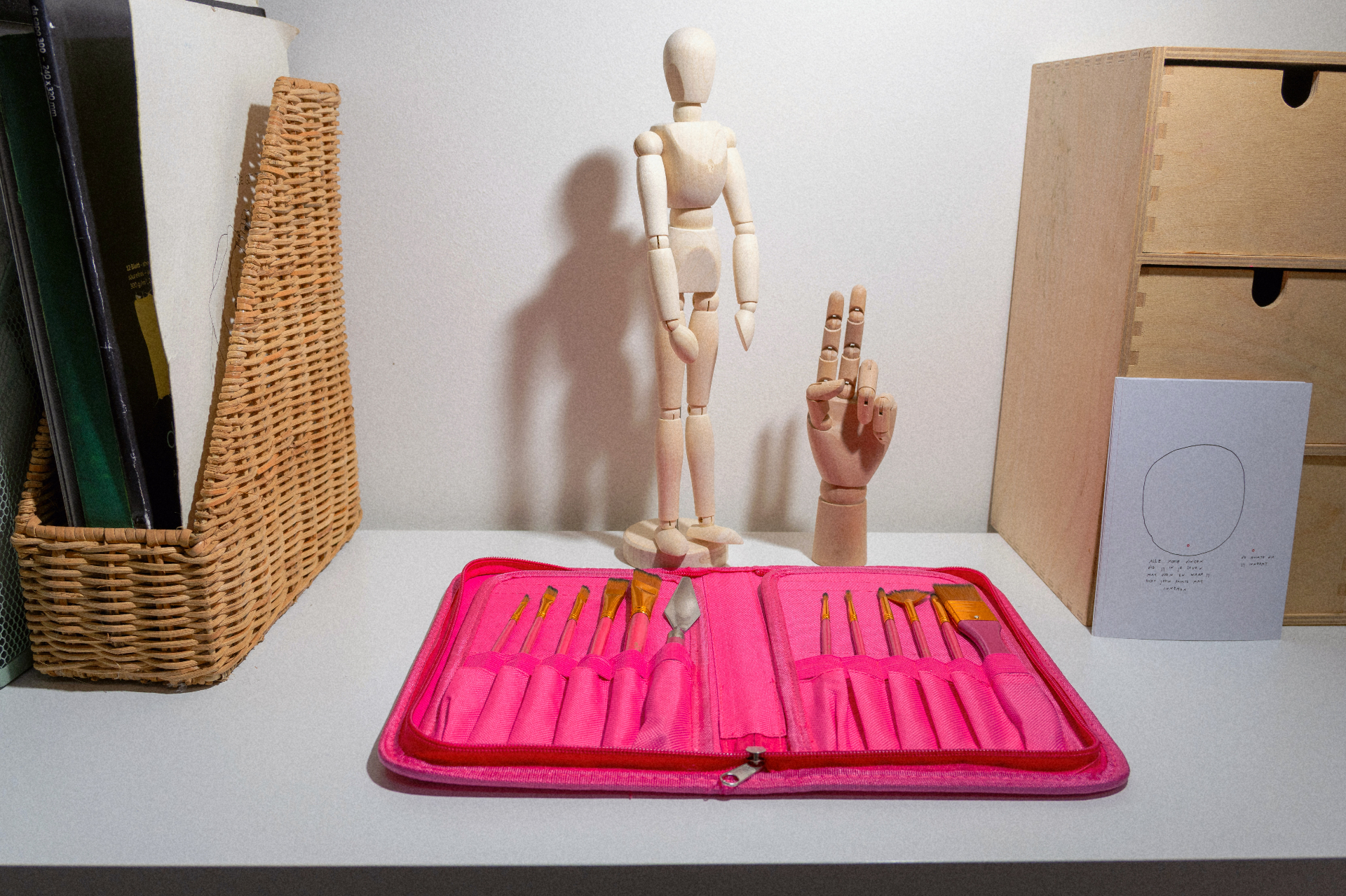 Houten tekenpop en handmodel naast een geopende etui met penselen in het atelier.